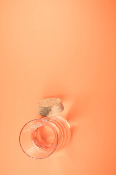 A vertical shot of a clear glass bottle with cork stopper isolated on an orange background - Foto, Imagem
