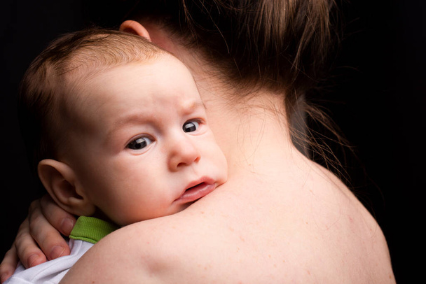 baby on mom's shoulder, looking at the camera, On a black background. - Fotoğraf, Görsel