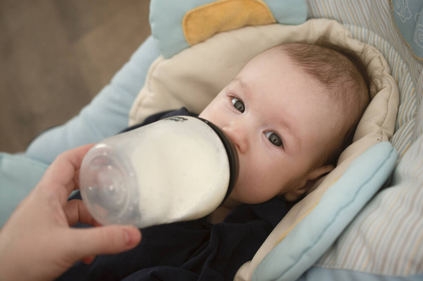 alimentando um bebê com uma mamadeira, o bebê olha para a câmera - Foto, Imagem