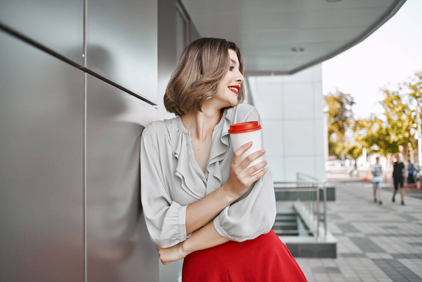 aantrekkelijke blonde vrouw in rode rok kopje drank buiten levensstijl - Foto, afbeelding