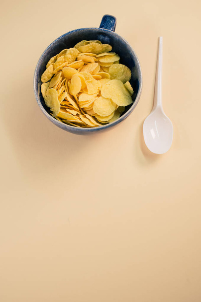 A vertical shot of corn flakes on a cup with plastic spoon isolated on brown background - Fotó, kép