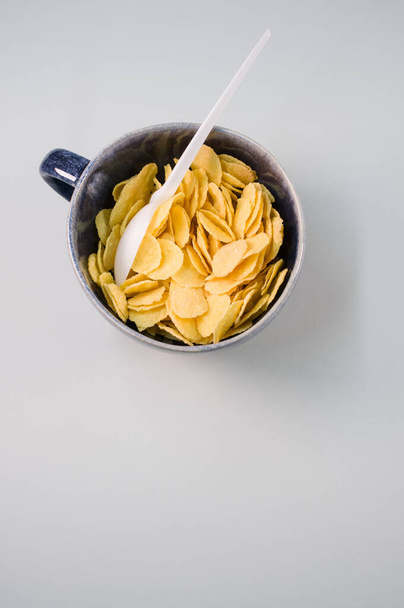 A vertical shot of corn flakes on a cup with plastic spoon isolated on a light gray background - Zdjęcie, obraz