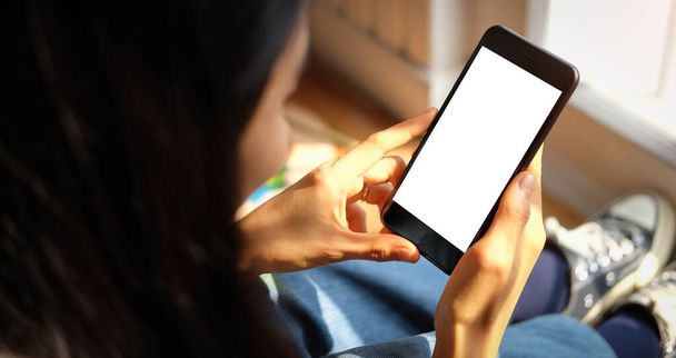 Обрезанный снимок женщины-художника с помощью мобильного телефона с пустым экраном, сидя перед полотном картины в ярко-белой студии. - Фото, изображение