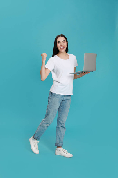 Emotional young woman with modern laptop on light blue background - Photo, Image