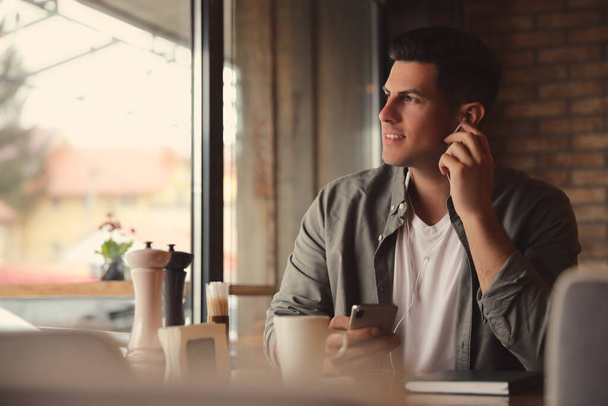 Hombre con smartphone escuchando audiolibro en la mesa en la cafetería - Foto, Imagen