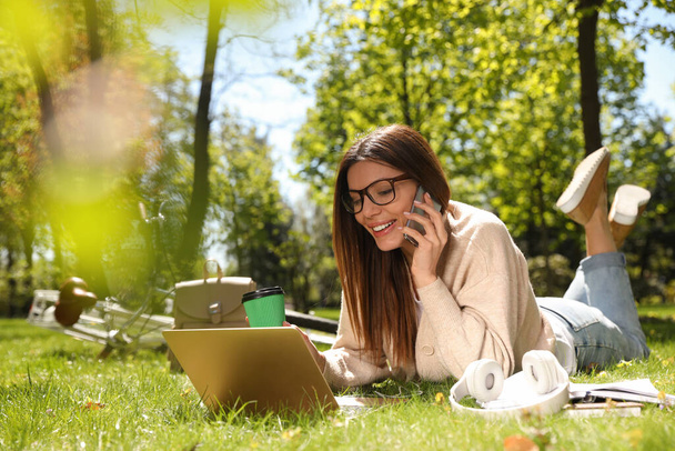 Femme parlant au téléphone tout en travaillant avec un ordinateur portable dans le parc - Photo, image