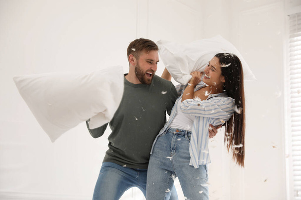 Happy young couple having fun pillow fight at home - Valokuva, kuva