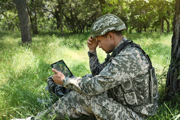 Солдат с рюкзаком с помощью планшета возле дерева в лесу - Фото, изображение