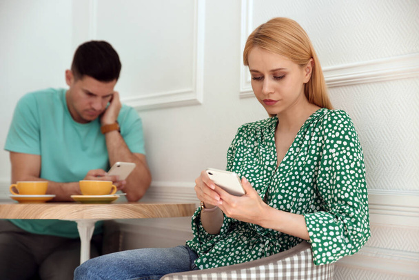 Man and young woman preferring smartphones over speaking with each other during first date in cafe - Photo, Image
