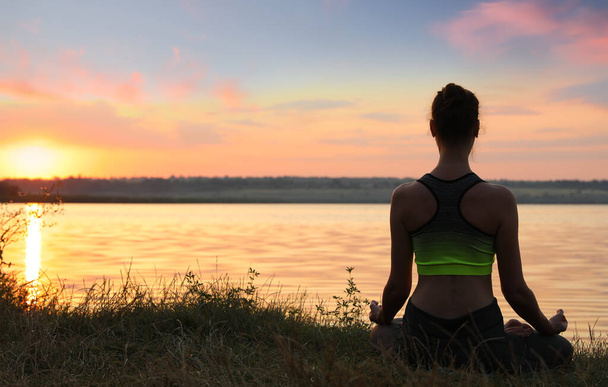 Woman meditating near river at sunset, back view. Space for text - Fotó, kép