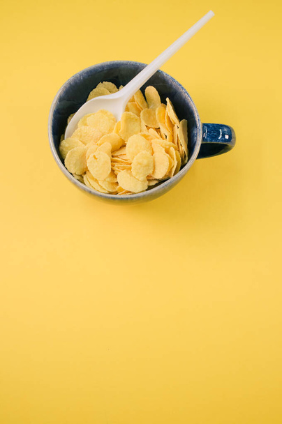 Um tiro vertical de flocos de milho em uma xícara com colher de plástico isolada em um fundo amarelo - Foto, Imagem