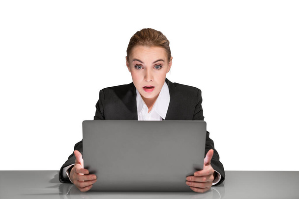 Portrait of attractive surprised young business woman in formal clothes sitting at the desk and looking on laptop display. Concept of corporate lifestyle. Hands hold computer. Isolated - Фото, изображение