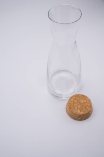 A vertical shot of a clear glass bottle with cork stopper isolated on a light gray background - Фото, изображение