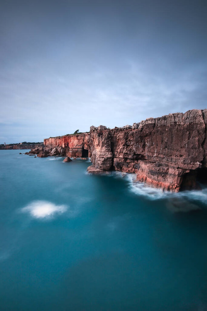 A vertical shot of the magnificent rocky cliffs over the endless ocean - Zdjęcie, obraz
