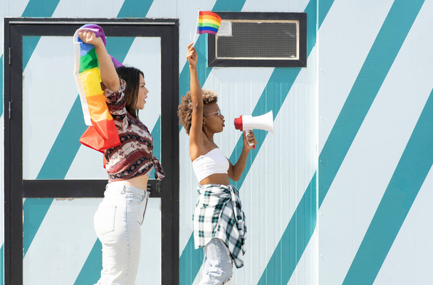 Eşcinsel gurur bayrağı ve megafonuyla, afro ve beyaz kadınlar eşitlik için gösteri yapıyorlar. - Fotoğraf, Görsel
