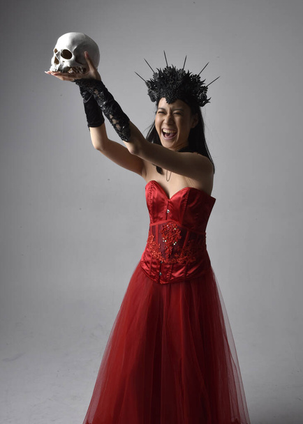 retrato de hermosa mujer asiática joven con corsé rojo y corona, posando en estilo de horror gótico con gestos creativos de la mano aislados sobre fondo negro oscuro estudio. - Foto, imagen