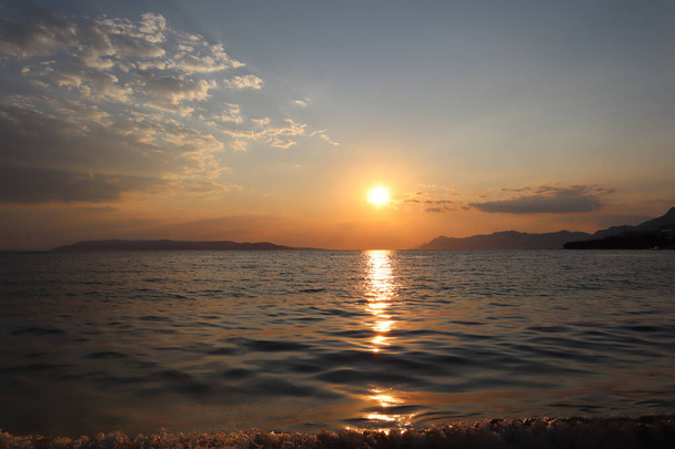 Paysage pittoresque du coucher de soleil sur la mer par une soirée d'été ensoleillée. Ciel orange et soleil, soleil éblouissant à la surface de la mer, panorama sur la côte croate, île de Brac à l'horizon - Photo, image