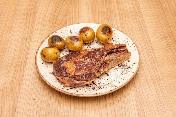Super entrecote z solą morską i sezonowych ziemniaków lub cachelos na białym talerzu i drewnianym stole - Zdjęcie, obraz
