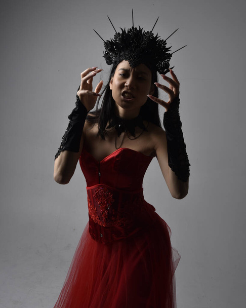 retrato de hermosa mujer asiática joven con corsé rojo y corona, posando en estilo de horror gótico con gestos creativos de la mano aislados sobre fondo negro oscuro estudio. - Foto, Imagen