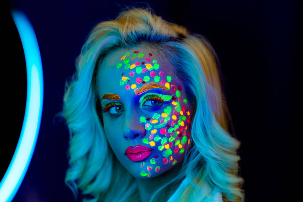 portrét ženy s malovanou tváří, žena s uv make-upem ve studiu, portrét ženy v karnevalové masce, žena je zdobena ultrafialovým práškem - Fotografie, Obrázek