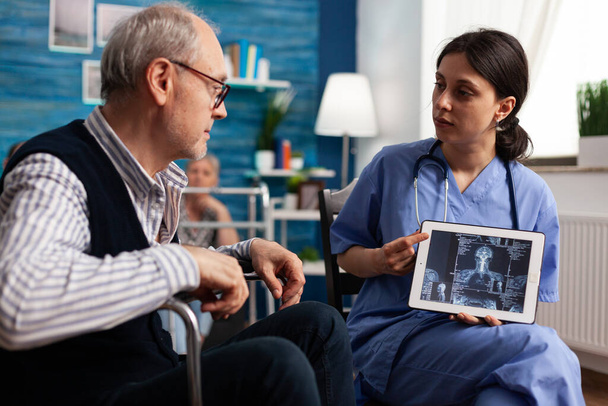 Enfermera social sosteniendo tableta con radiografía en exhibición explicando tratamiento médico - Foto, Imagen