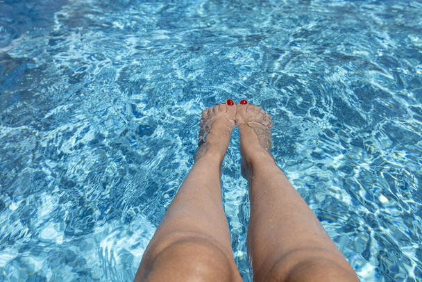 A woman's legs in the clear water of a swimming pool - Foto, Imagen