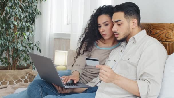Spanish arabian married couple millennials man and woman wife and husband boyfriend and girlfriend consumers use laptop for online shopping ordering goods over internet enter number from bank card - Footage, Video
