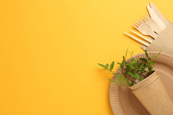 Flat lay of paper and wooden tableware with green twigs on yellow background, space for text. Eco friendly lifestyle - Fotó, kép