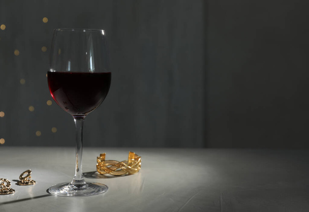 Glass of red wine and jewelry on white table against blurred festive lights, space for text - Fotografie, Obrázek