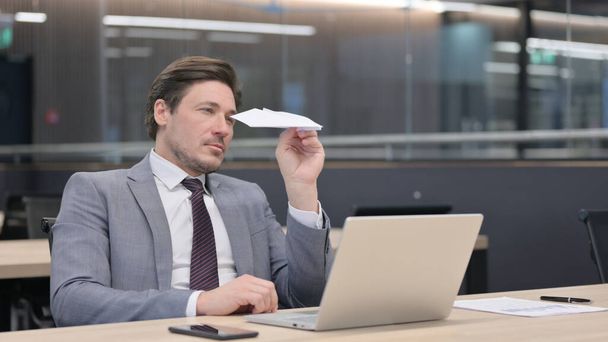 Hombre de negocios de mediana edad que vuela avión de papel mientras está en la oficina - Foto, imagen