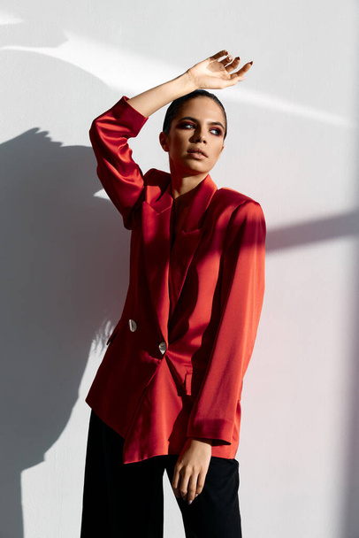 fashionable woman in a red jacket and black trousers hold her hand above her head - Photo, Image