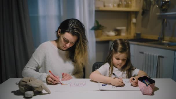 Äiti ja pieni tytär piirtävät piirroksia paperille keittiössä merkkiaineilla - Materiaali, video