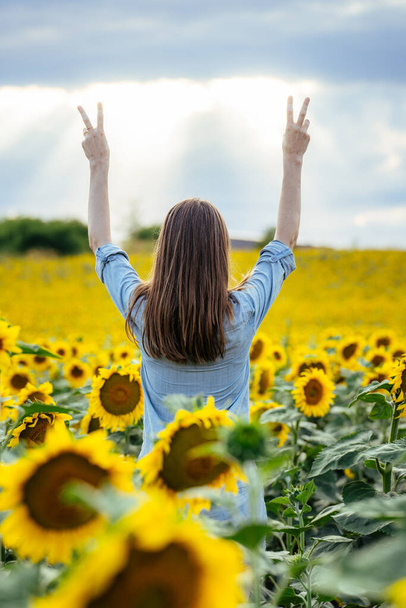 Una mujer levantando los brazos con las manos en un signo de paz en un soleado campo de girasol, Freedom Peace Lifestyle Outdoor Concept - Foto, imagen