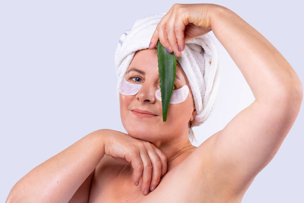 Afbeelding van een mooie met naakte schouders volwassen vrouw poseren met de aloë blad in haar hand, zorgt voor het gezicht huid. - Foto, afbeelding