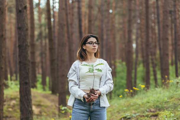 Young female volunteer plants a forest, holding an oak tree seedling in her hands - Фото, зображення