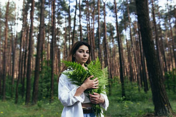 A woman in the woods hugs a bouquet of ferns, a young activist protects the forest - Фото, изображение