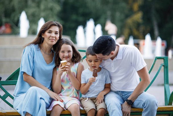 Famiglia che mangia gelato su una panchina nel parco estivo. Focus selettivo, sfondo sfocato. Buona infanzia. Cura dei genitori. - Foto, immagini