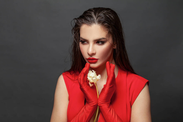 Valentine's Day. Loving woman. Beautiful female model in a red dress on black. Red lipstick makeup on the lips from the beautiful lady. - Photo, Image