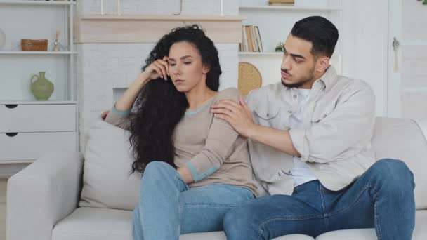 Obrażony zdenerwowany zmartwiony Hiszpanka żona uczucie smutny stres troskliwy mąż arabski Hiszpan mężczyzna facet konsole wspiera przeprosiny, małżeństwo po konflikcie siedzi na kanapie w domu - Materiał filmowy, wideo