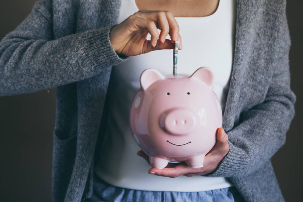 Close-up young woman putting bill in piggy bank. Female saving money for household payments, bank bills, calculating monthly family budgets, making investments or strategy for retirement. - Foto, Imagen