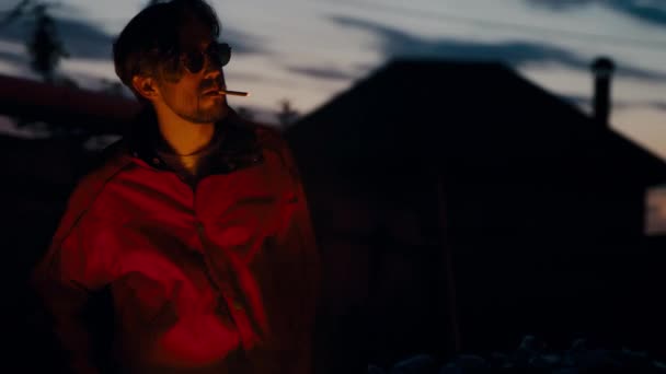 Mann mit Brille und roter Jacke sonnt sich neben brennendem Mülleimer im Gesicht. - Filmmaterial, Video