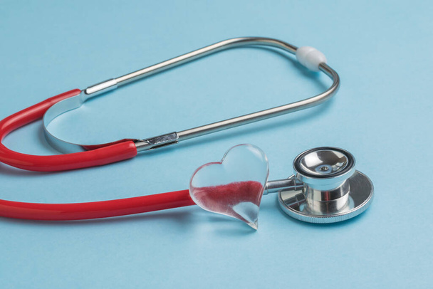 Ein gläsernes Herz und ein rotes Stethoskop auf blauem Hintergrund. Das Konzept der Behandlung verschiedener Krankheiten. - Foto, Bild
