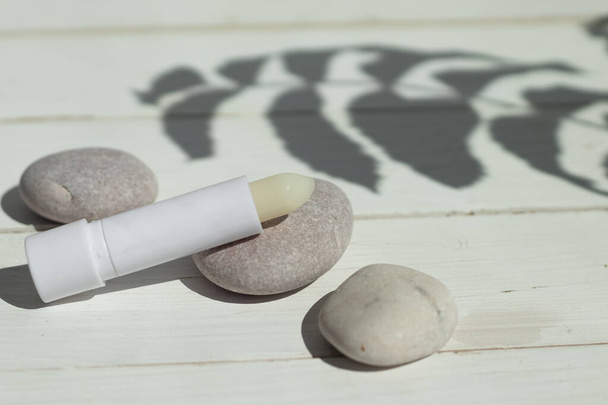 hygienic lipstick on a white wooden background hard shadows, decorate the stones. - Fotoğraf, Görsel
