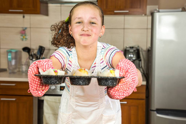Το κοριτσάκι ψήνει κεκάκια στο σπίτι, ετοιμάζει πρωινό ή σνακ στο σχολείο - Φωτογραφία, εικόνα