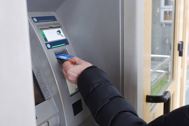 Ένας άνθρωπος χέρι εισάγει μια πιστωτική κάρτα σε ένα μηχάνημα ΑΤΜ. - Φωτογραφία, εικόνα