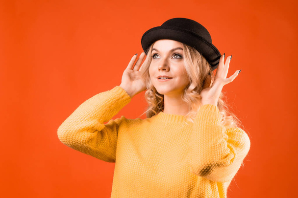 Stylish young woman in knitted clothes and bowler hat, bright orange background - Photo, Image