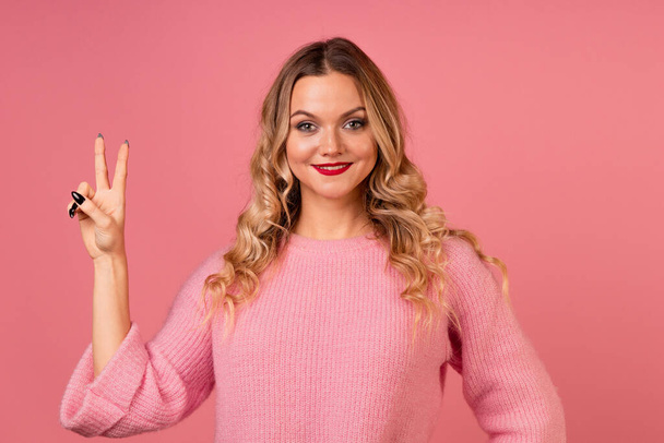 A young, attractive woman in a warm pink sweater makes hand gestures. - Foto, Imagem