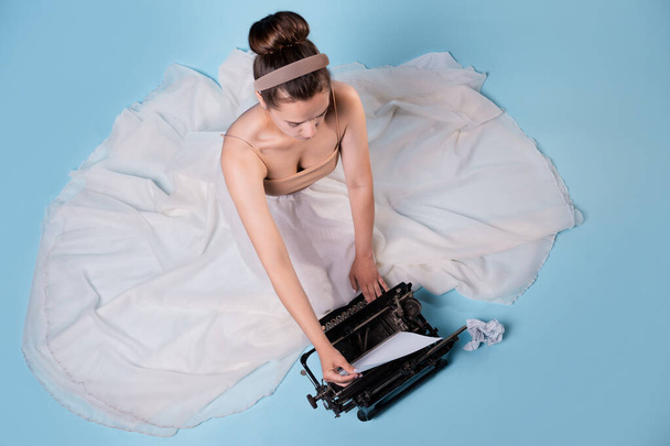 young romantic woman is an author at a typewriter, sitting on the floor in a fluffy white skirt - Foto, immagini