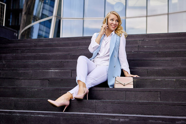 Happy woman in business suit talks by cellphone on stairs. - Фото, изображение