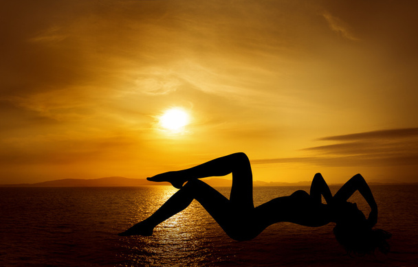 Mujer silueta sexy sobre el cielo puesta de sol en el mar
 - Foto, imagen